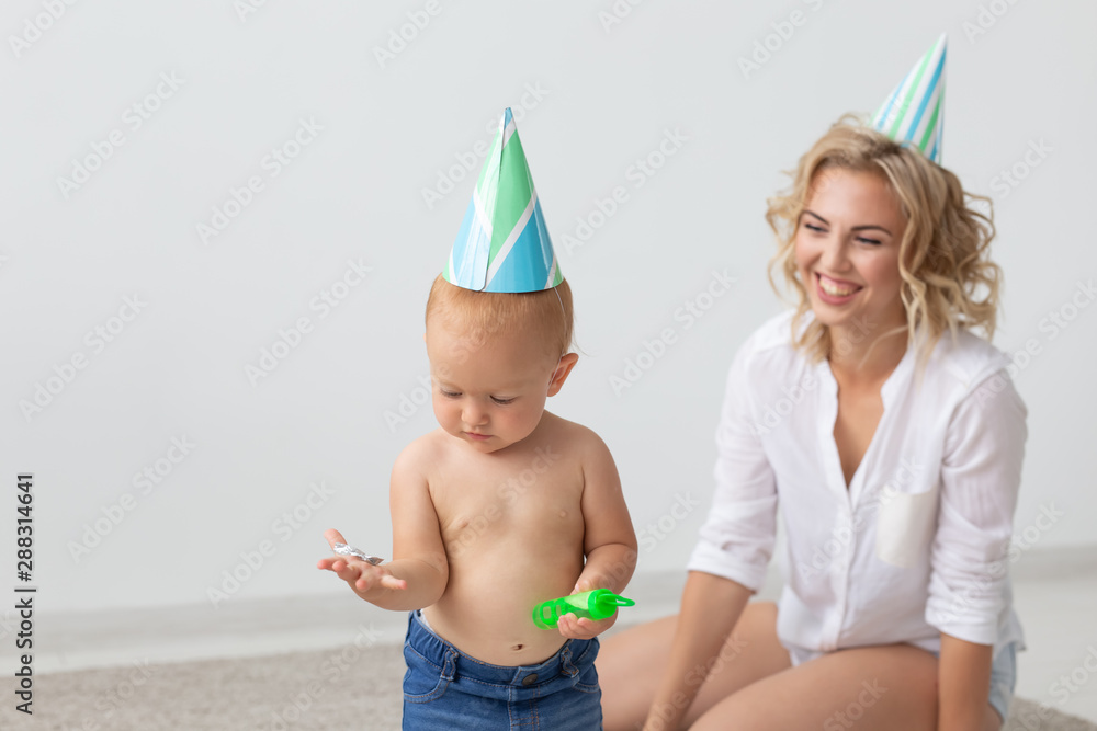Young smiling mother and cute little daughter in birthday caps spending time together on carpet at home. Family holidays and values