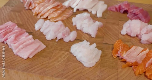 Slow pan across a beautiful presentation of fresh sliced sashimi fish on a wooden board sitting in the middle of wooden table. Fish includes raw tuna, salmon and snapper photo