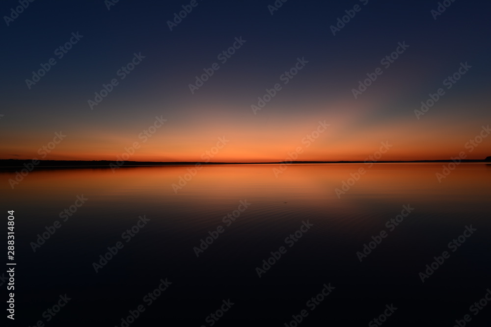 Bright blue sky in pink with a red twilight glow on the horizon over water