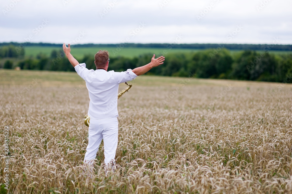 saxophonist in a white suit stands in the field. Flight of the soul, philosophy of freedom saxophonist in a white suit stands in the field. Flight of the soul, philosophy of freedom