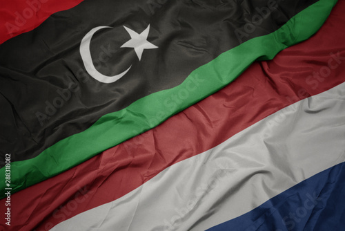waving colorful flag of netherlands and national flag of libya.