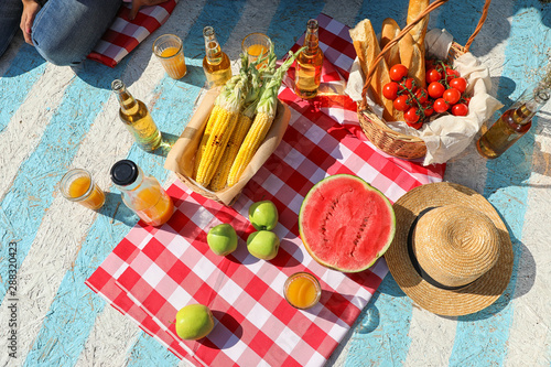 Straw hat and different products for summer picnic on checkered blanket, flat lay