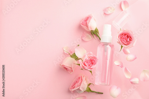 Flat lay composition with rose essential oil and flowers on pink background, space for text