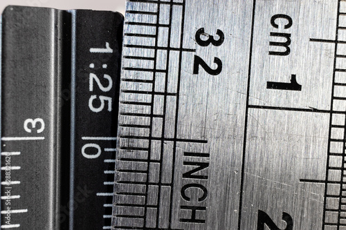 Close-up picture of two steel rulers showing the size difference between inches and centimeters. Conceptual british and metric system comparison.