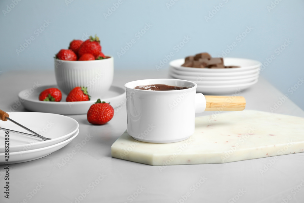 Fondue pot with chocolate and strawberry on grey table Fondue pot with chocolate and strawberry on grey table