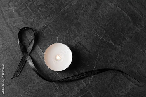 Black ribbon and burning candle on dark grey stone surface, top view. Funeral symbols