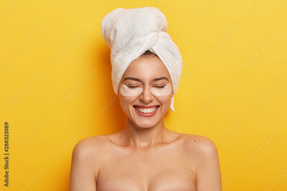 Headshot of satisfied beautiful naked woman applies white patches under