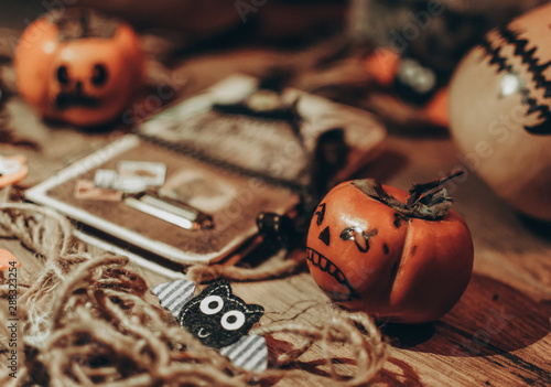 Halloween little pumpkin with painted faces on a wooden floor, next to it is a notebook with bats, handmade work preparing for the holiday. © Алла Морозова