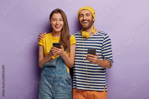 Happy young woman and man embrace and have fun, use modern technologies, hold...