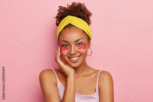 Photo Portrait of smiling Afro American woman with under eye patches, relieves puffine