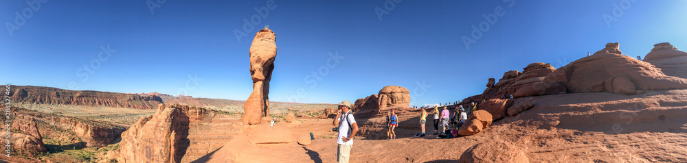 ARCHES NATIONAL PARK, USA - JULY 2, 2019: Panoramic view of Delicate Arch and tourists ARCHES NATIONAL PARK, USA - JULY 2, 2019: Panoramic view of Delicate Arch and tourists