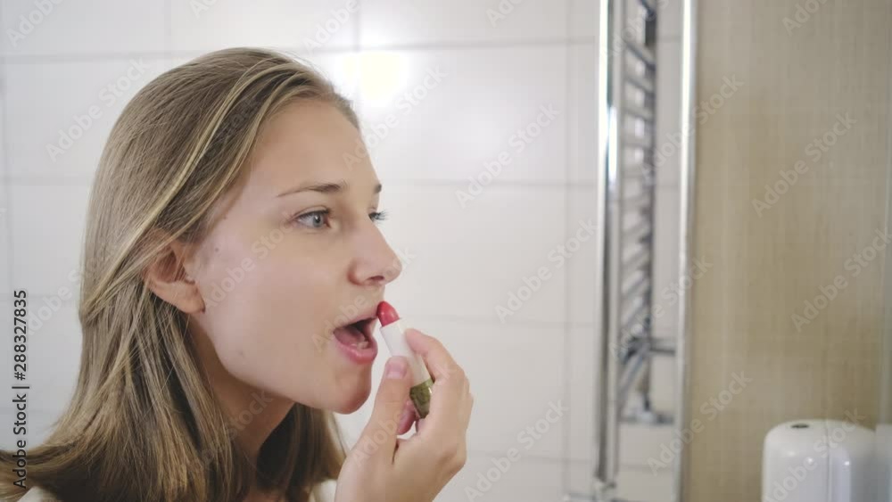 blond girl puts on red lipstick in bathroom