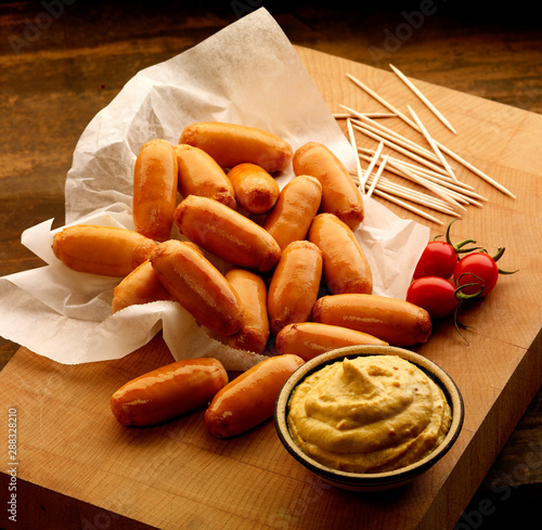 Pile of Cocktails sausages on wooden board with mustard