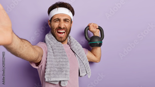 Photo Glad smiling man with toothy smile, wears white headband, lifts heavy weight, ta
