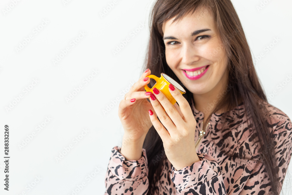 Cute young woman holding a small toy yellow mug in her hands posing on a white background with copy space. Favorite drinks concept