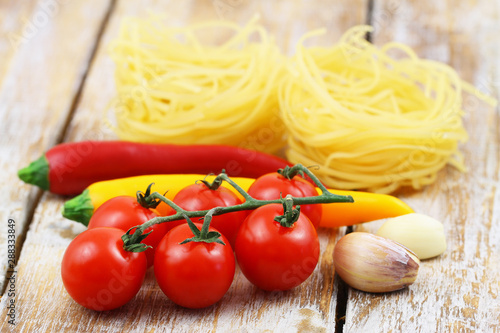 Selection of cooking ingredients: tagliatelle, cherry tomatoes, garlic cloves and chilies on wooden surface