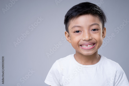 An Asian boy smiling wearing a white t-shirt on a grey background. 