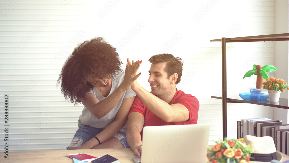 Diversity couple high five after booking Summer trip deal on internet Diversity couple high five after booking Summer trip deal on internet