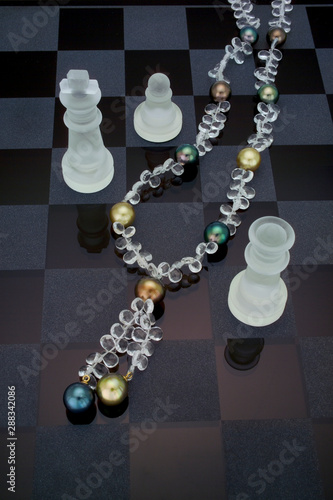 A necklace of Tahitian pearls and crystal bead make up this necklace laying on a chess board.