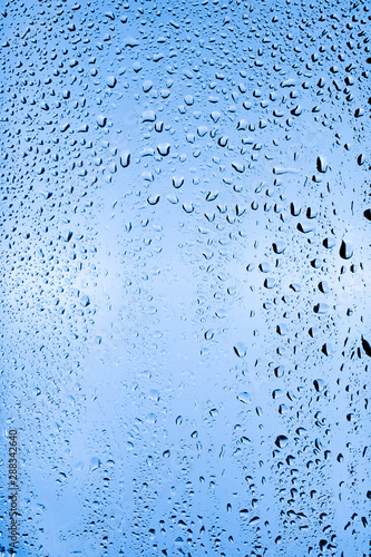 Drops of water flow down a transparent glass on a blue background. 