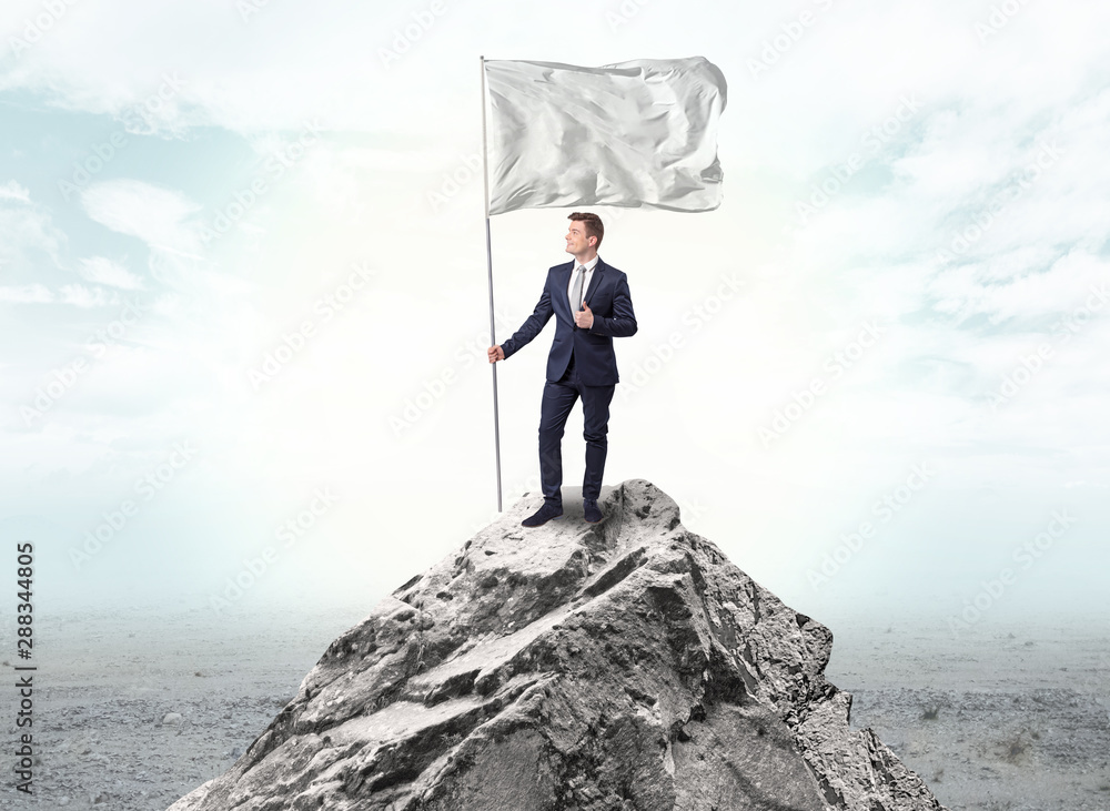 Obraz premium Handsome businessman on the top of the mountain with white flag