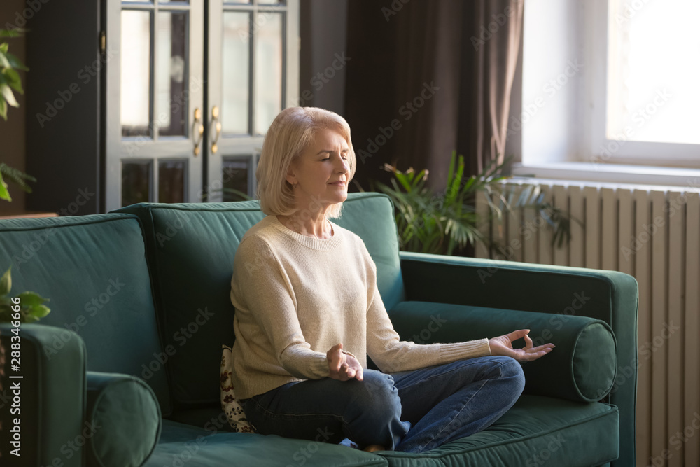 Calm senior woman meditating on couch at home Calm senior woman meditating on couch at home