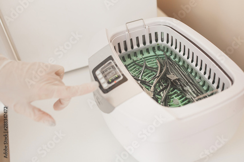 Manicurist sterilize her tools in the autoclave or oven. Master int he salon preparing her instruments for disinfection.