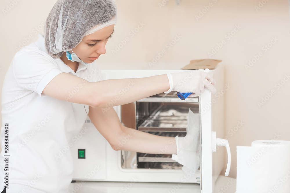 Manicurist sterilize her tools in the autoclave or oven. Master int he salon preparing her instruments for disinfection.