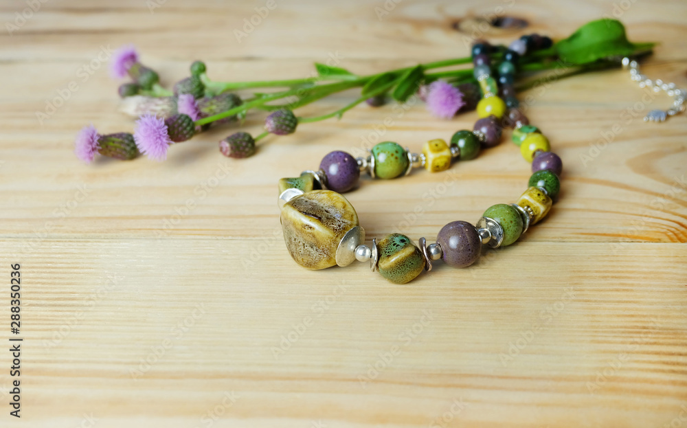 Φωτογραφία Beads from ceramics and natural stones and thistle flowers on a wooden table, composition with handmade jewelry