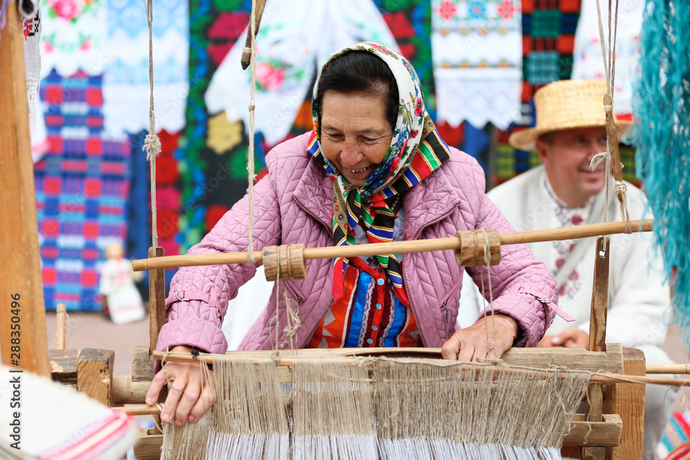 Grandmother works behind an old spinning machine.Spice on an old spinning wheel. Ancient fabrication. Woman weaver