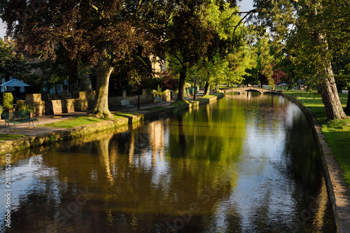 Early morning sun on River Windrush with reflected trees and sleeping ducks in Bourton-on-the-Water village in the Cotswolds England photo