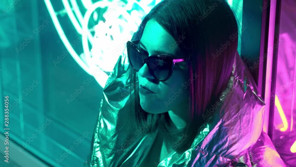 Young fashion teen girl in fur glasses blowing bubble gum illuminated with street neon blue pink sign, beautiful millennial woman in trendy night light glow back to 80s concept. Young fashion teen girl in fur glasses blowing bubble gum illuminated with street neon blue pink sign, beautiful millennial woman in trendy night light glow back to 80s concept.