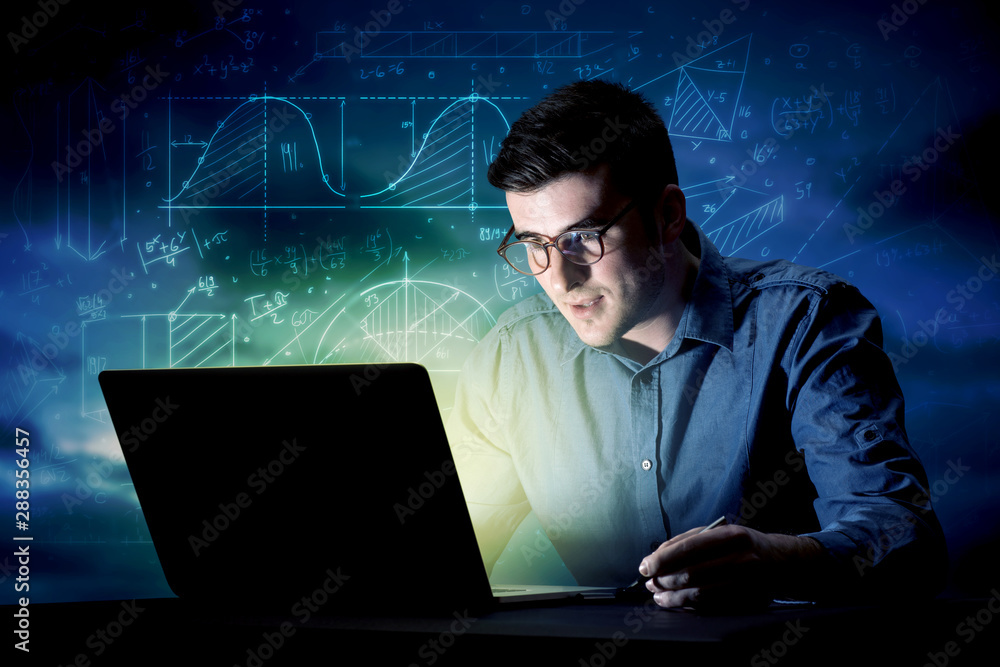 Young handsome businessman working late at night in the office with blue mathematic charts in the background Young handsome businessman working late at night in the office with blue mathematic charts in the background