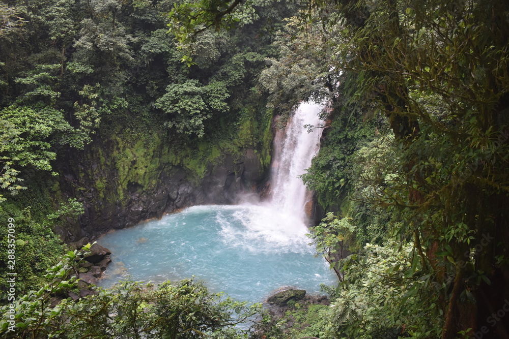 Obraz premium Beautiful waterfall of turquoise blue water, surrounded by green tropical vegetation.