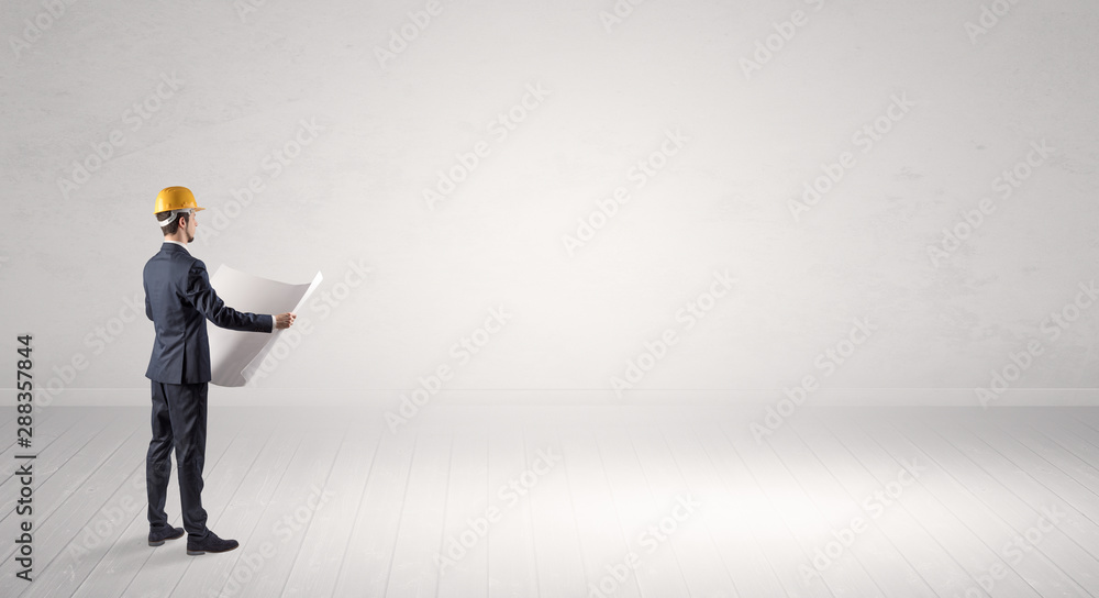 Young architect with construction helmet standing in an empty space and holding a plan Young architect with construction helmet standing in an empty space and holding a plan