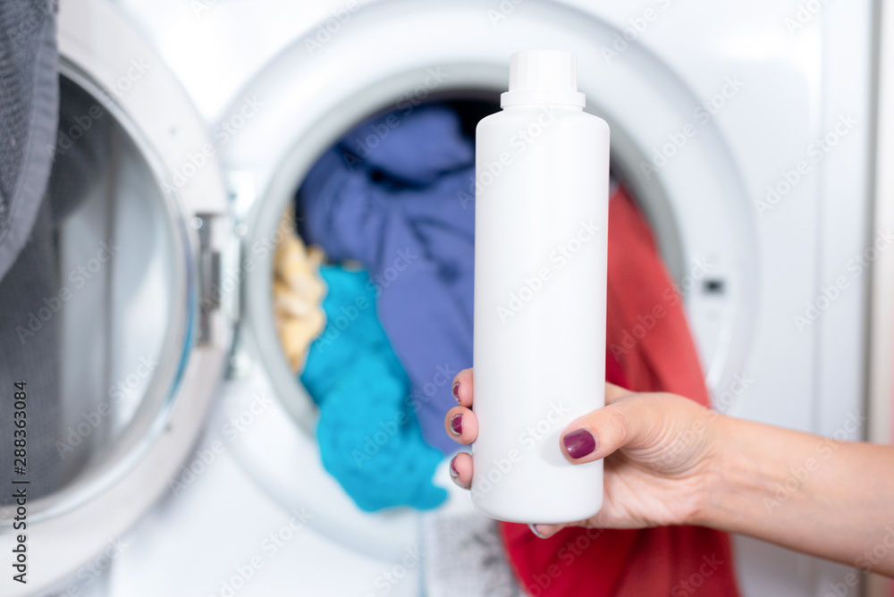 Woman is holding in hands a liquid laundry detergent on a washing machine background. Woman is holding in hands a liquid laundry detergent on a washing machine background.