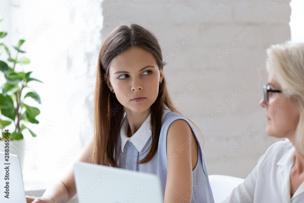 Serious female employee look angry at woman colleague in office Serious female employee look angry at woman colleague in office
