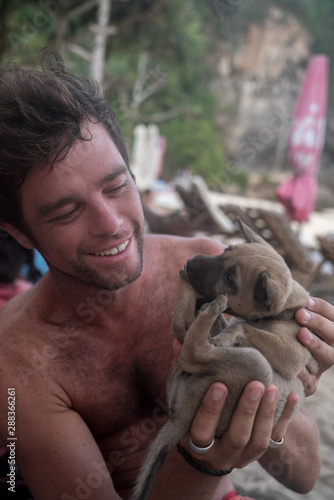 Young guy smiling and playing with a cute small puppy at a beach