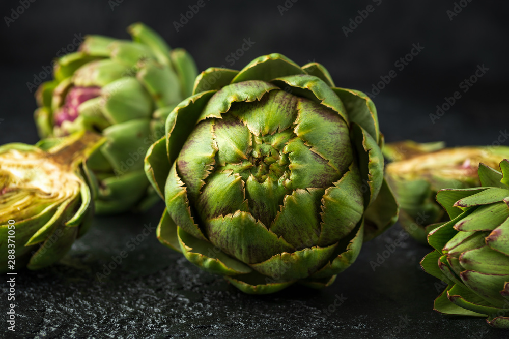 Fototapeta premium Fresh raw organically grown artichoke flower buds on dark background