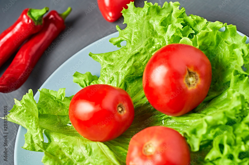 Fresh green fluffy leaves of salad lettuce, red pepper, tomato, plate lies on scratched dark concrete. Vegetarian, dieting, healthy, low calorie food Fresh green fluffy leaves of salad lettuce, red pepper, tomato, plate lies on scratched dark concrete. Vegetarian, dieting, healthy, low calorie food