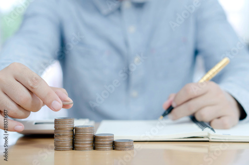 Business man putting coin on pile of money saving bank and account for his money all in finance accounting concept.