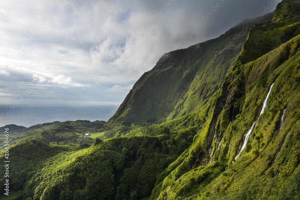 Fototapeta premium aerial landscape image of sunset sunrise over Poço Ribeira do Ferreiro waterfalls with its remarkable amazing tropical like green vegetation and forests at the Ilha das Flores island on the Azores