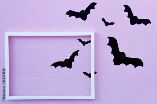 black paper bats and white frame on pink background. top view. happy Halloween.