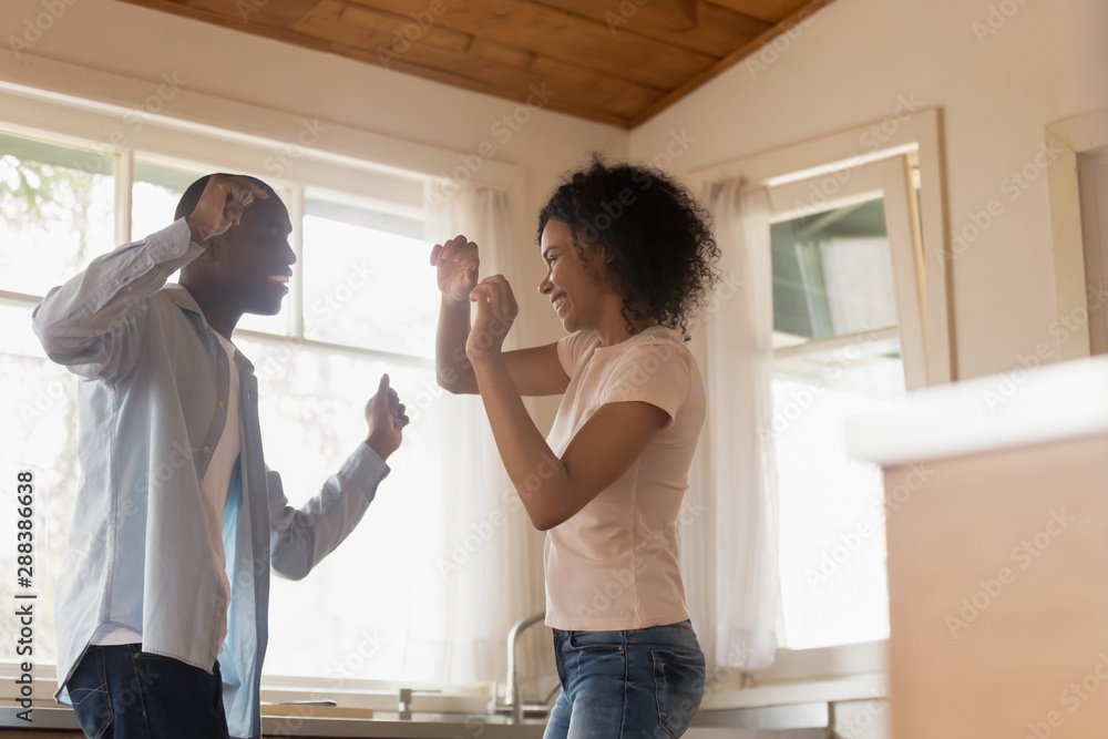 Obraz premium Happy biracial couple dancing in kitchen celebrating relocation