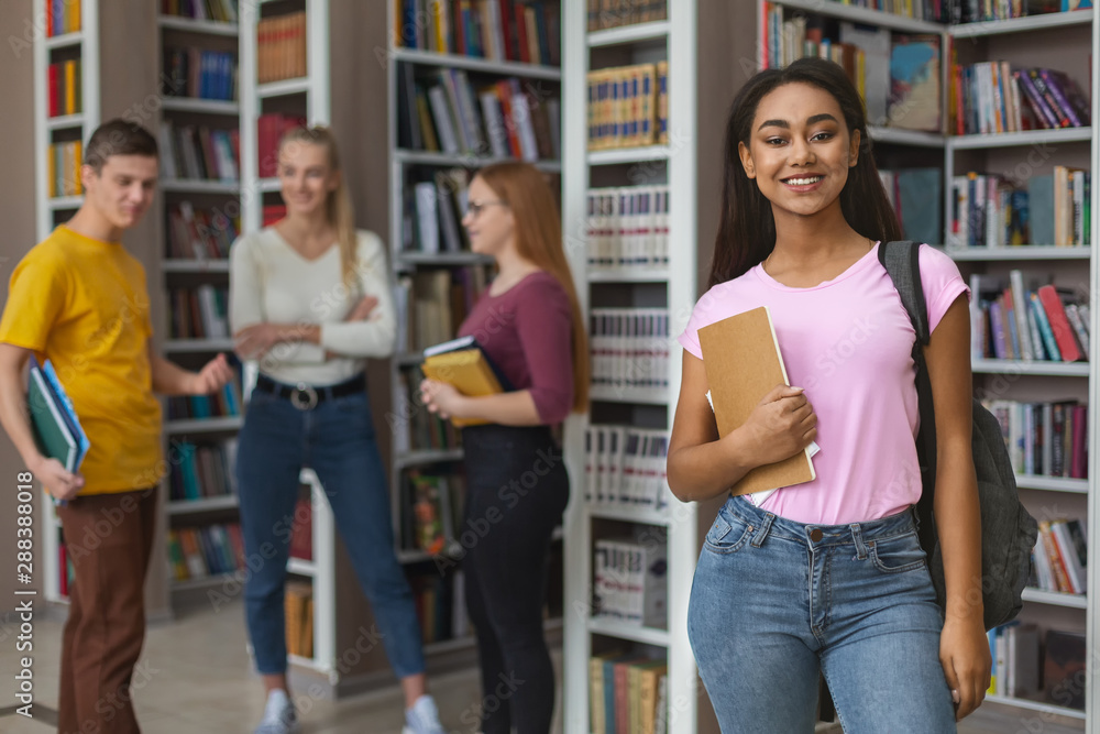Cheerful african american girl posing next to bookshelves in library Cheerful african american girl posing next to bookshelves in library