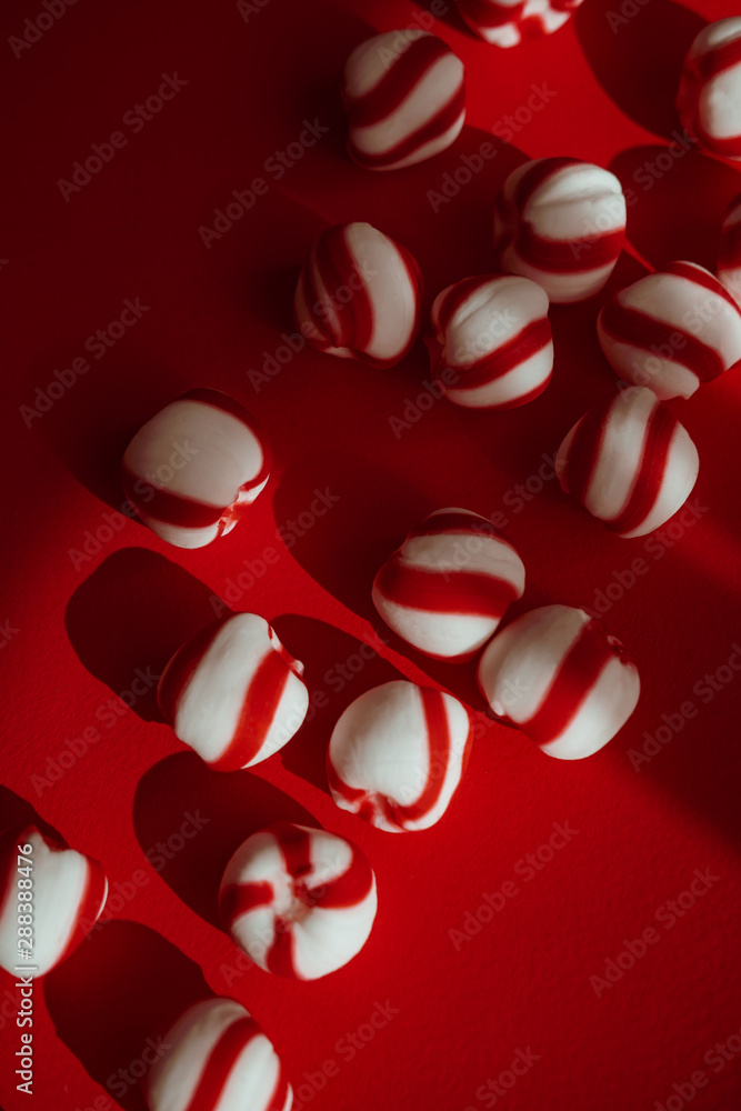 Peppermint candies on red background. Direct sun light, focus on shadows. Winter, New Year, Christmas seasonal minimalism still life, flat lay. Vertical Peppermint candies on red background. Direct sun light, focus on shadows. Winter, New Year, Christmas seasonal minimalism still life, flat lay. Vertical