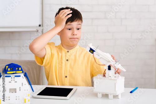 Stem education. Dismayed boy creating robot and made mistake photo