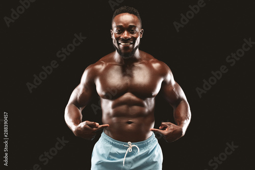 Smiling african fitness model pointing at his six packs