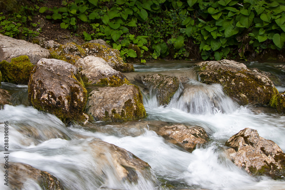 A stream of water flows over stones with green moss, naturalness in nature. Small picturesque waterfall . A stream of water flows over stones with green moss, naturalness in nature. Small picturesque waterfall .