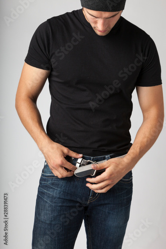Healthy, slim, slender young man wearing black t-shirt, jeans and knit hat putting on a belt fastening buckle. Young men's modern casual clothing fashions styles, diet, fitness and weight loss.